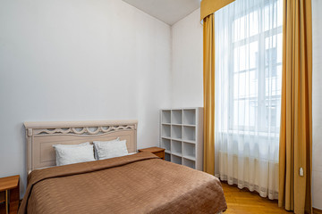 View of bed and window with curtain in bedroom interior. White walls.