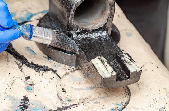 Hand in blue rubber gloves paints metal parts of an old vise with black paint with a brush