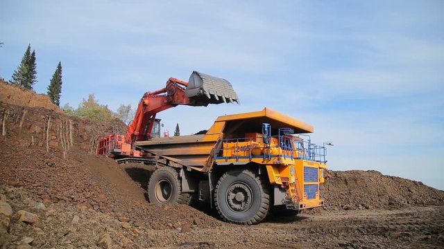 Red excavator loads tipper truck