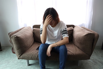 Asian woman stressful face with her hands cover of face. Short hair asian Woman feel lonely and sad sit alone on sofa bed in the living room