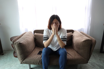Asian woman stressful face with her hands cover of face. Short hair asian Woman feel lonely and sad sit alone on sofa bed in the living room