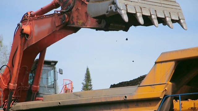 Close-up Red excavator digs an earth and loads into a yellow dump truck