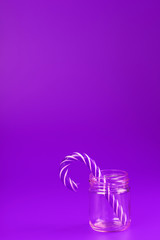 One Lollipop Candy cane in a glass jar on a purple background.