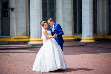  bride and groom dancing among the white columns  in a sunny day