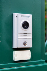 an intercom with a video camera and a microphone for voice communication with a card reader for access by a key card is installed on a green iron gate side view.