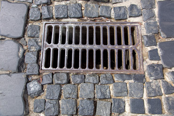 the iron grate of the drainage system hatch on the road paved with paving stones, closeup of a sewer grate top view.