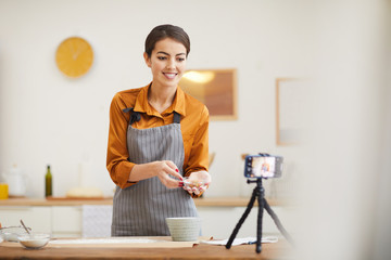 Waist up portrait of beautiful young woman smiling at camera while filming baking tutorial for video channel, copy space - obrazy, fototapety, plakaty