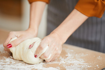 Close up of unrecognizable woman kneading batter while baking homemade pastry on kitchen table, copy space