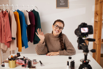 Portrait of smiling young woman waving at camera while filming video for beauty and lifestyle...