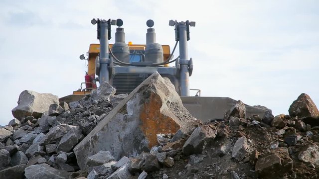 Yellow tracked bulldozer moves bucket stones on camera. Focus on stones
