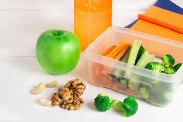 School lunch box with a sandwich, vegetables, water, almonds and fruit on a white Board. Healthy eating concept - background layout with free text space. The flat composition lay on top .