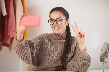 Portrait of contemporary young woman wearing glasses taking selfie photo via smartphone while...