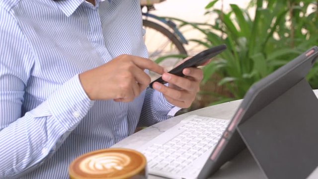 Asian businesswoman using smartphone and typing digital tablet in the cafe