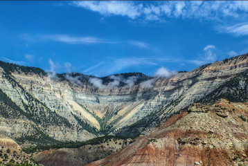 Beautiful eroded mountains showing layers and a valley with trees - white rocks in the distance and red up close with layers and fog at the top under beautiful sky