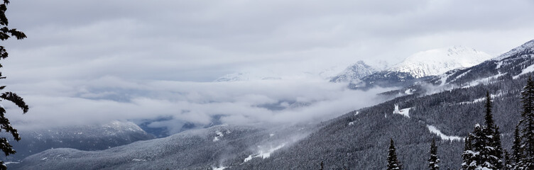 Obraz premium Whistler, British Columbia, Canada. Beautiful Panoramic View of the Canadian Snow Covered Mountain Landscape during a cloudy and foggy winter day.