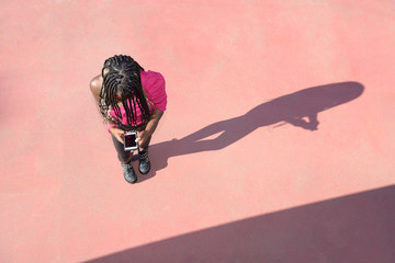 Happy afro-style black girl with long black and blondes braids wearing sunglasses stands on a red floor while uses her telephone and earphones