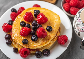 Sweet homemade pancakes with raspberries on white plate on grey table.