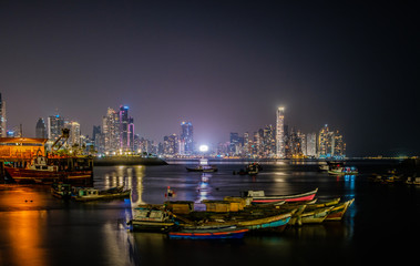 Fototapeta na wymiar boats and city skyline at night - cityscape of Panama City business district - illuminated skyscraper buildings ,