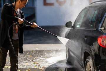 Young man washing car cleaning with foam and hi pressured water
