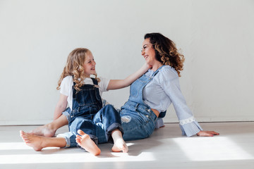 Mom with little girl in denim jumpsuit play in white room