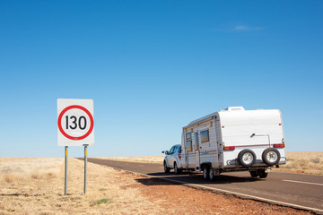 Road showing 130kms/hr sign while car with caravan drives by.