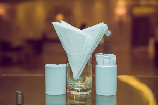 White Napkins In A Metal Napkin Holder, Spices Salt And Pepper On A Woodeglass Table, Panoramic View. Toothpick . A Table In A Cafe Or Restaurant.