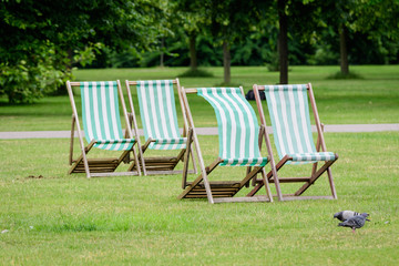 Four white and green striped outdoor garden chairs displayed in fresh green grass in a park in London, Great Britain, during a windy summer day, natural green background in a big city