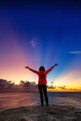 Adventurous Girl with open hands on a Rocky Ocean Coast enjoying the beautiful view of the Colorful Sunset. Image Composit. Adventure, Travel, Explore, Freedom Concept.