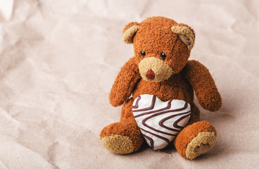 A toy Teddy bear with a gingerbread heart on a brown paper background.Space for text