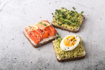 Open sandwiches with avocado, red fish, egg and micro greenery. Light gray background.
