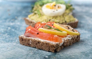 Open sandwiches with avocado, red fish on a blue stone background. Close-up