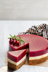 Delicious layered cranberry cheese cake on white wooden table