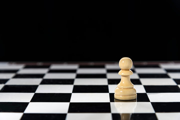 White stand-alone chess pawn on a chess table, black background