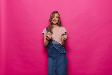 Fototapeta premium Portrait of happy smiling woman posing with credit card and mobile phone after online shopping on isolated pink background. Happy girl in denim clothes posing in professional studio.
