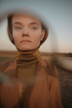 Young female portrait through magnifying glass in nature