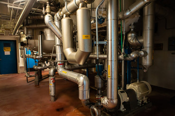 the piping system under tanks and vessels, metallic stainless steel pipes and pumps, with signs of hot caution, wort pre-syrup, syrup injection, steam