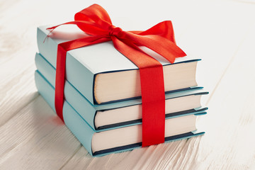 Fototapeta premium A stack of three books tied with a red ribbon with a bow: the concept of a good book - a good gift