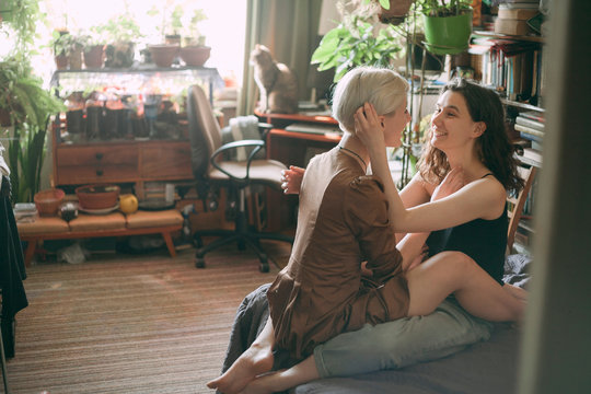 TWO GIRLS OF LESBIANS WITH WARM LIGHT IN A ROOM, SIT CLOSELY FRIEND TO A FRIEND on the sofa in the room