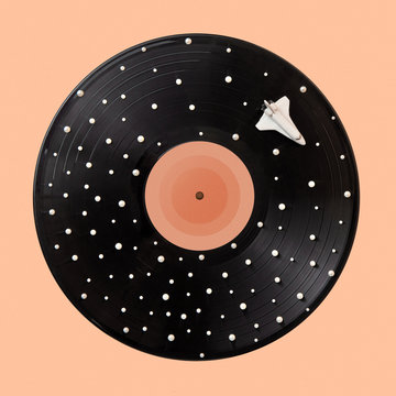 Black vinyl record with white spots stars and space ship on a beige background.