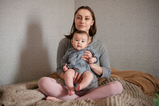 mother with a newborn baby sitting on a bed in the lotus position
