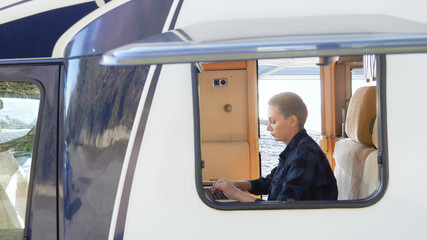 A woman uses a laptop while sitting at a table in a motor home.