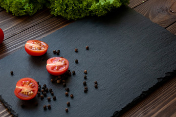 Fresh tomatoes, salad and pepper for use as cooking ingredients on the black desk. Text space.