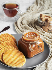Homemade salted caramel sauce in a glass jar on a rustic wooden table. Close-up. Round caramel...