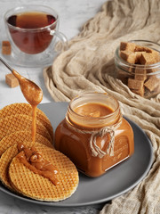 A spoon with carmel sauce pours wafers on a plate. Close-up. Jar of homemade caramel sauce. Selective Focus, Vertical Orientation