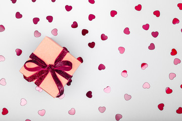 Craft box with dark red velvet ribbon bow and glitter heart confetti. Valentine day and eco-friendly wrapping concept. Trendy minimalistic flat lay design background. Horizontal