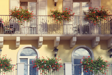 Fototapeta na wymiar Tall windows on an balcony with flowers in Italy, Riva city in summer at sunrise
