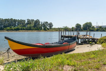 Obraz premium Traditional fishing boat on the shore of Ria de Aveiro near a small wooden jetty. Portuguese landscape.