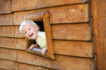 Curious child, toddler boy, peering from a small window in wooden shrub