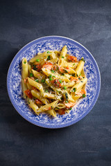 Creamy salmon penne pasta with parmesan cheese green peas in blue bowl on gray background