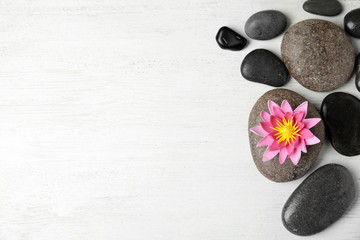 Fototapeta na wymiar Stones with lotus flower and space for text on white wooden background, flat lay. Zen lifestyle